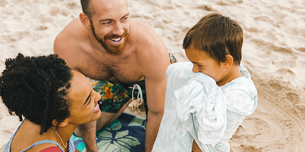 Família composta por pai, mãe e filho pequeno aproveitando as férias na praia