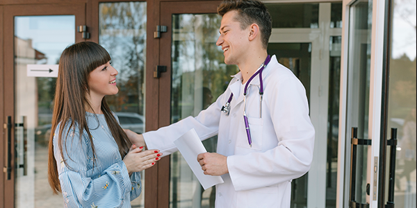 médico com estetoscópio roxo cumprimentando paciente com encaixe de consulta na porta do consultório